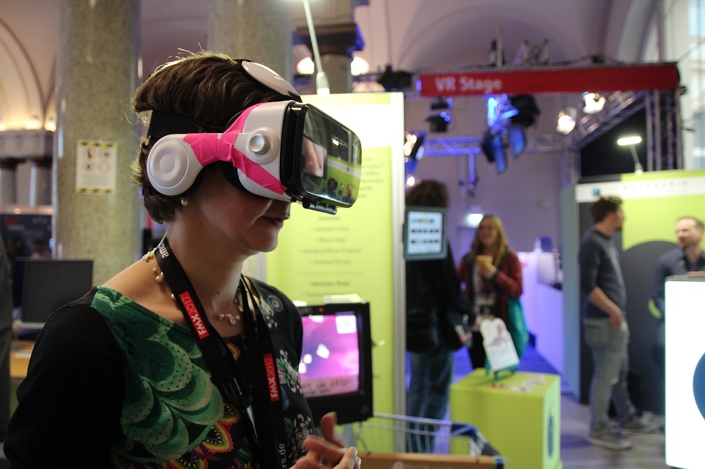 Raksta autore Elīna Reitere ar "Virtuālās Realitātes brillēm", izbaudot Bādenes-Virtembergas Kinoakadēmijas transmediju nozares studenta Maestro Pivetta studiju projektu "VR Pigeons": ar VR brillēm uz deguna jātēlo balodis, kas knābā baltmaizi. Maizes kumosi bija ieraugāmi virtuālajā vidē un, kratot galvu un imitējot knābāšanu, tos varēja "apēst". Izklaidējoši...